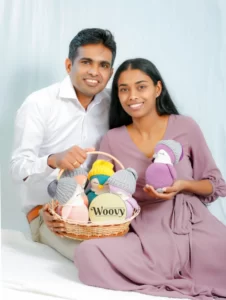 A woman with blonde hair wearing a white shirt holds two crochet bunnies, one light blue and one pink, in her hands.