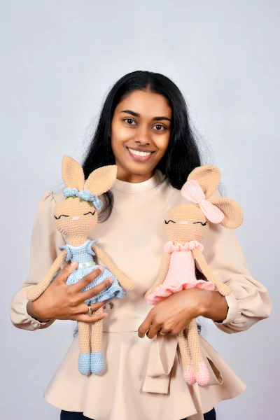A woman holding two adorable Woovy Crochet Bunny Ballerinas, one in a baby pink dress and the other in a baby blue dress.