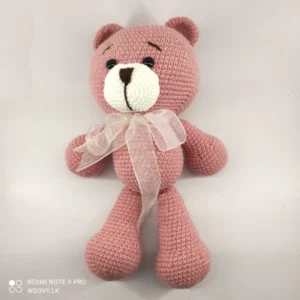 A close-up image of the Woovy Crochet Amigurumi Salmon Pink Teddy Bear with White Bow, made from soft crochet materials and featuring adorable details like a cute nose and button eyes.