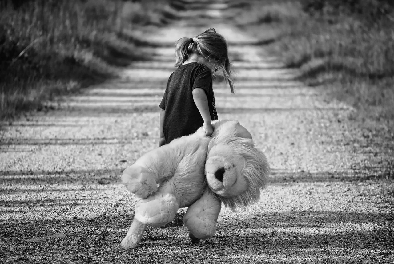 A young girl carrying a teddy bear with a smile on her face.