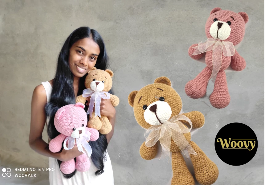 A woman holding two Woovy Crochet Amigurumi Teddy Bears, one brown and one salmon pink, with embroidered eyes and cute outfits.