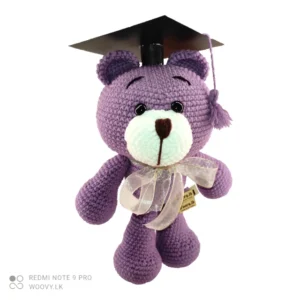 A close-up of the Woovy Crochet Graduation Bear, showcasing its adorable design with a graduation cap and gown. The bear is made of soft crochet material and has embroidered eyes and a friendly smile.